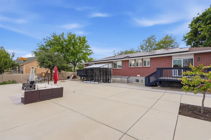 Expansive concrete patio with a brick exterior, elevated dark wood deck, and solar panels