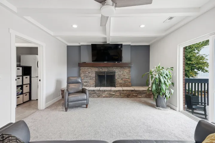 Coffered ceiling with a ceiling fan, stone fireplace with a wood-finish mantel, and a sliding glass door