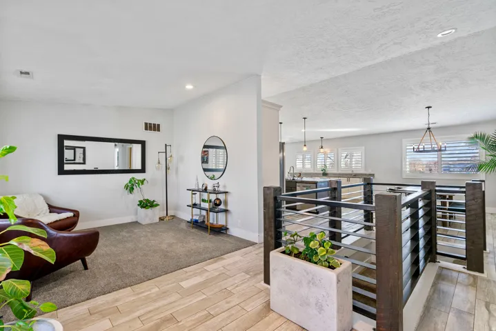 Open-concept living space featuring wood-finish flooring, recessed lighting, and a modern staircase with horizontal metal balusters