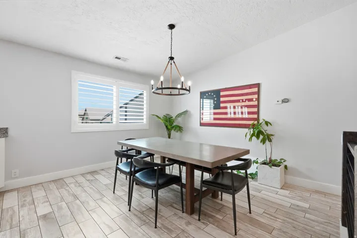 Light wood-finish flooring, white plantation shutters, and a modern chandelier