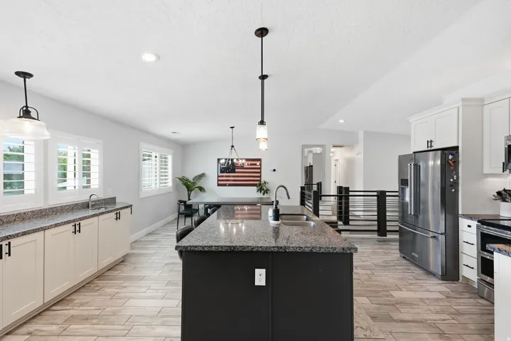 Gourmet kitchen featuring a large center island with black cabinetry, stainless steel appliances, quartz countertops, pendant lighting, white perimeter cabinetry, wood-finish flooring, and abundant natural light from multiple windows