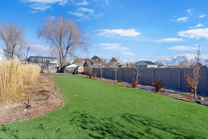 Expansive lawn with artificial turf, mature trees, a privacy fence, and mountain scenery