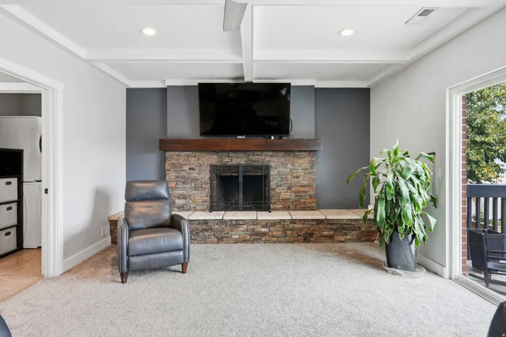 Stone-clad fireplace with a wood mantle, coffered ceiling, recessed lighting, and sliding glass door