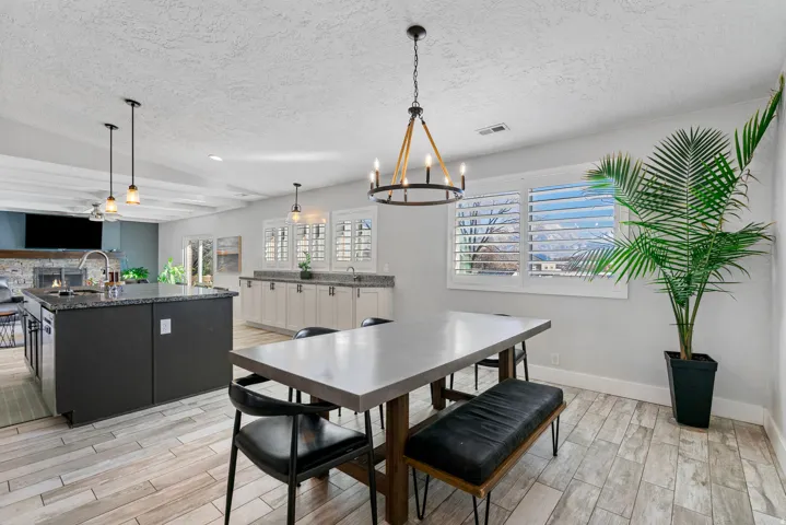 Spacious kitchen and dining area featuring wood-finish flooring, a large island with a stone countertop, and pendant lighting