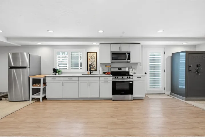 Modern kitchen featuring stainless steel appliances, white cabinetry with ample storage, black gas range with built-in microwave, wood-finish flooring throughout, and recessed ceiling lighting
