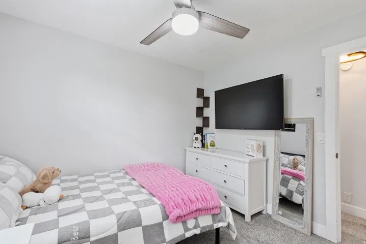 Comfortable bedroom featuring a ceiling fan with integrated lighting, carpeted flooring, and a white dresser with ample storage