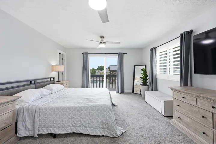 Spacious primary bedroom with ensuite access to a private balcony, ceiling fan, and abundant natural light