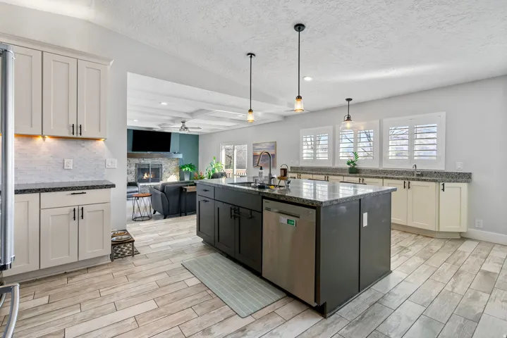 Kitchen featuring a dark-toned island with granite-style countertop, stainless steel dishwasher, light-toned perimeter cabinetry with granite-style countertops, and wood-finish flooring