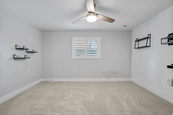 Carpeted flooring, window with white plantation shutters, white trim, and a ceiling fan with integrated lighting