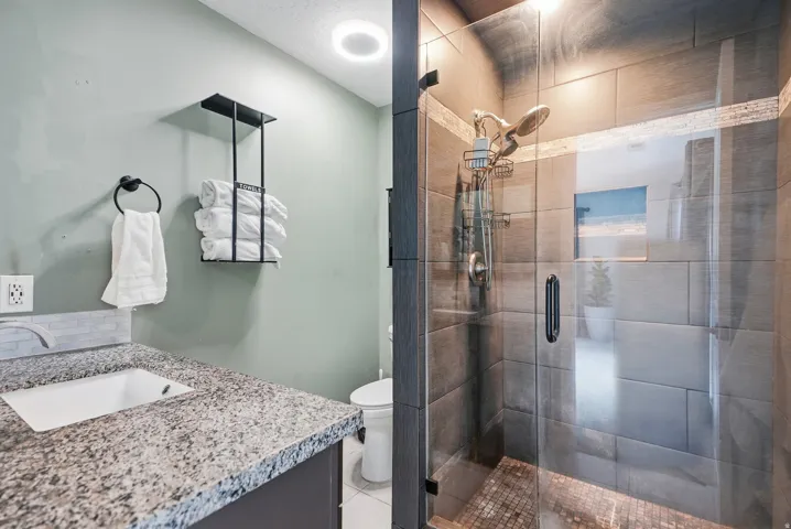 Granite-look countertop with an undermount sink, mosaic tile backsplash, and a glass-enclosed shower featuring large format tile walls and a mosaic tile floor