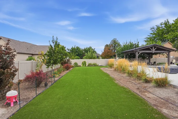Expansive backyard oasis featuring a lush, manicured lawn, mature landscaping with seasonal plantings, fenced perimeter for privacy, covered pergola structure, and decorative hardscaping with ornamental grasses along the rear border