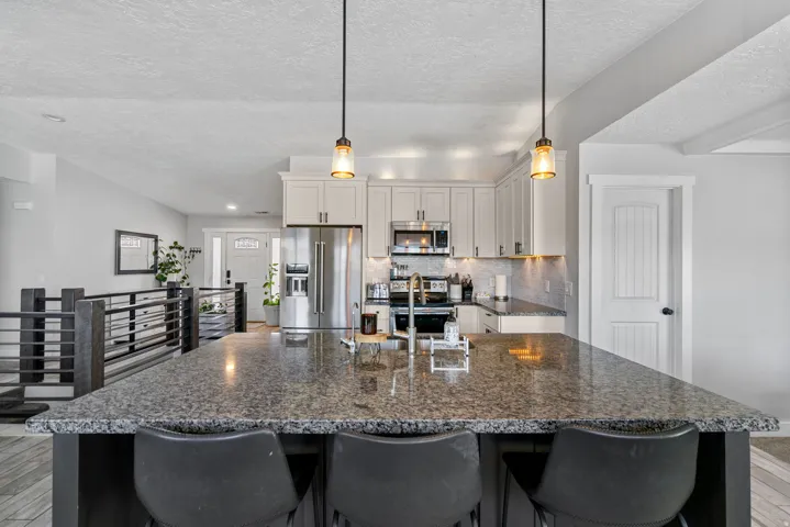 Kitchen featuring a large island with a stone countertop, light-toned cabinetry, stainless steel appliances, and pendant lighting
