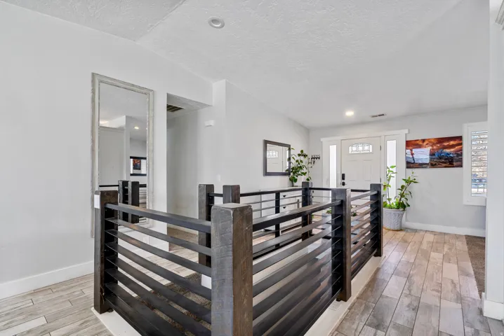 Entryway featuring wood-finish flooring, a white paneled front door with decorative glass, and a contemporary dark wood and metal railing