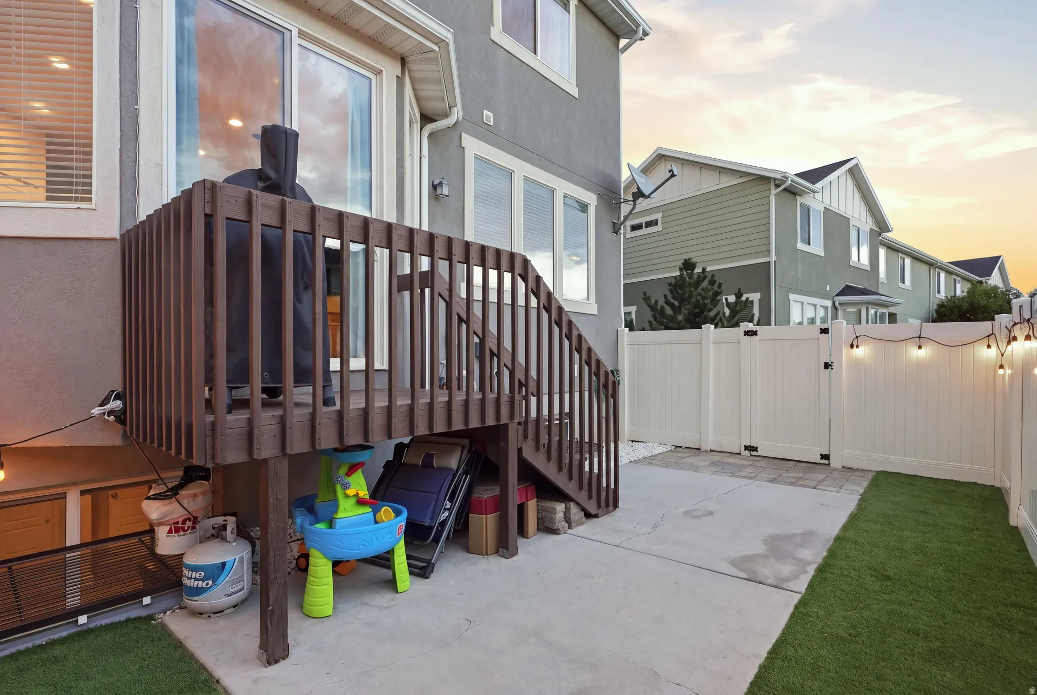 Elevated wood-tone deck with stairs, private fenced yard, concrete patio, and artificial turf