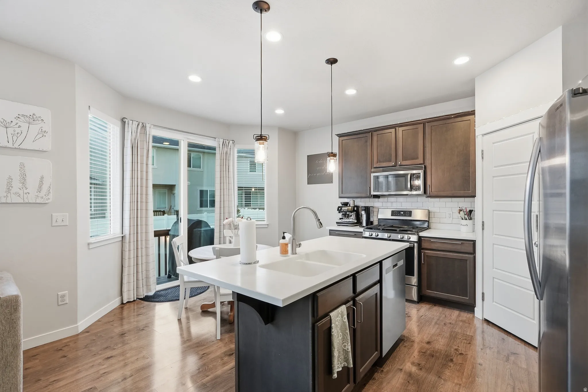Kitchen featuring a center island with dual sinks, dark wood-finish cabinetry, stainless steel appliances, and wood-finish flooring