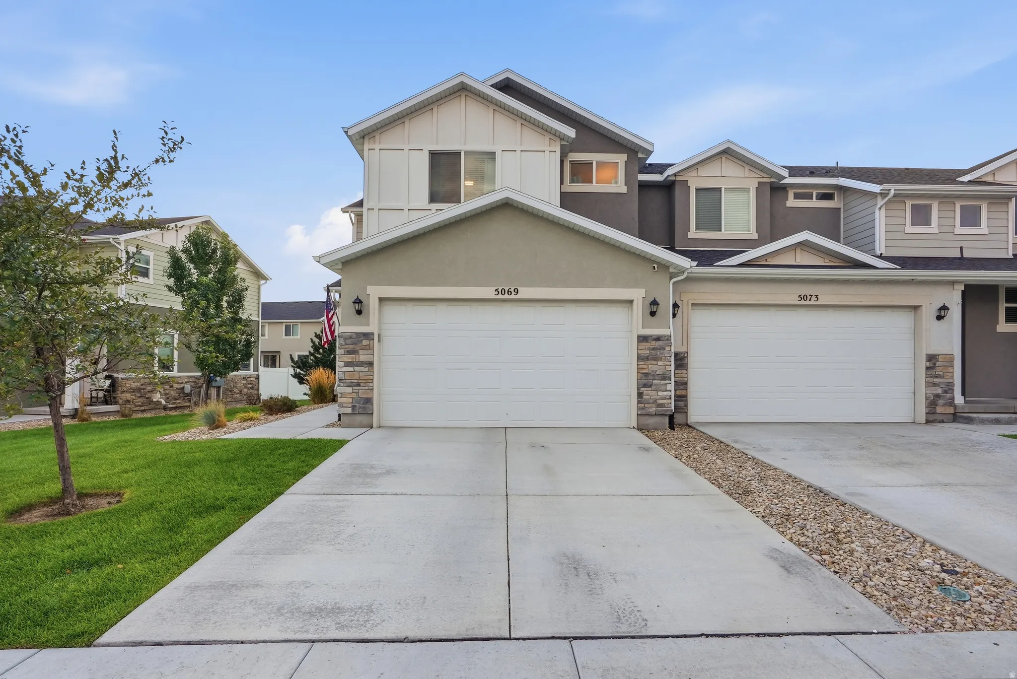 Stucco exterior with stone accents, two-car garage, concrete driveway, and manicured lawn