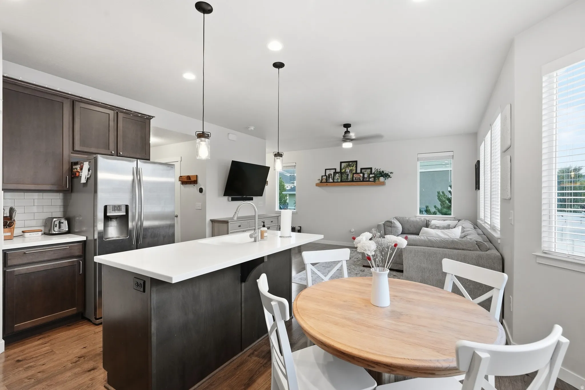 Open-concept living space with wood-finish flooring, white countertops, dark cabinetry, and multiple windows