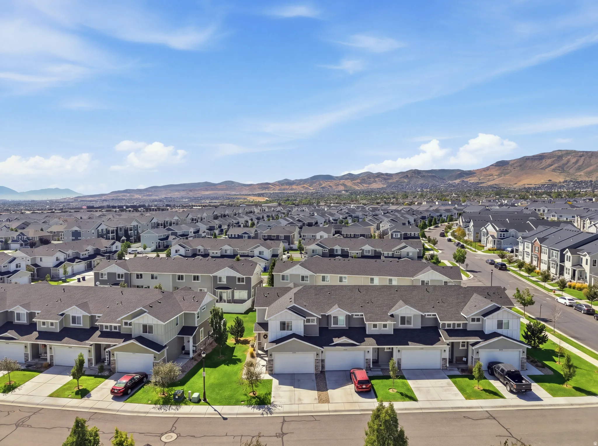 Residential community with a mountain backdrop, featuring multiple two-story homes with attached garages, paved driveways, and landscaped front yards