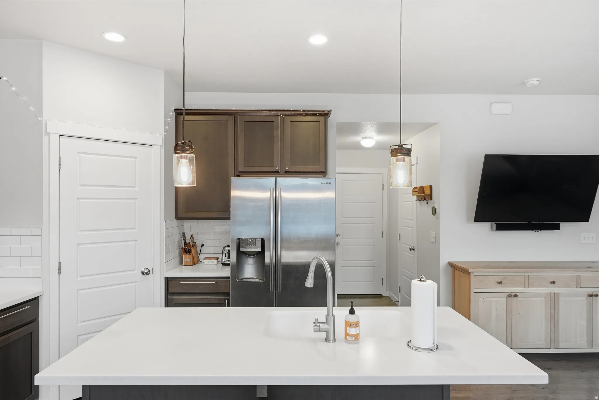 Kitchen featuring a stainless steel refrigerator, white subway tile backsplash, dark wood-finish cabinetry, and a center island with a white countertop