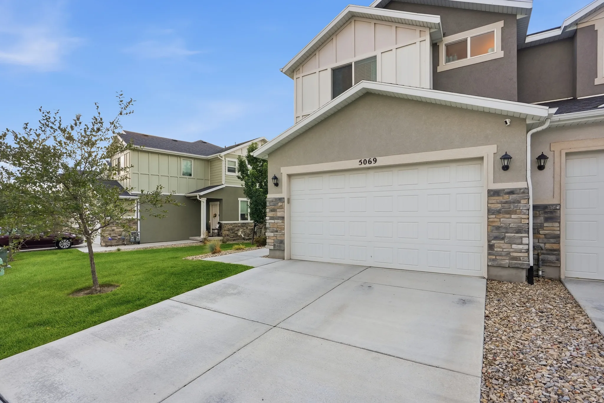 Stucco exterior featuring stacked stone accents, two attached garage doors, and a concrete driveway