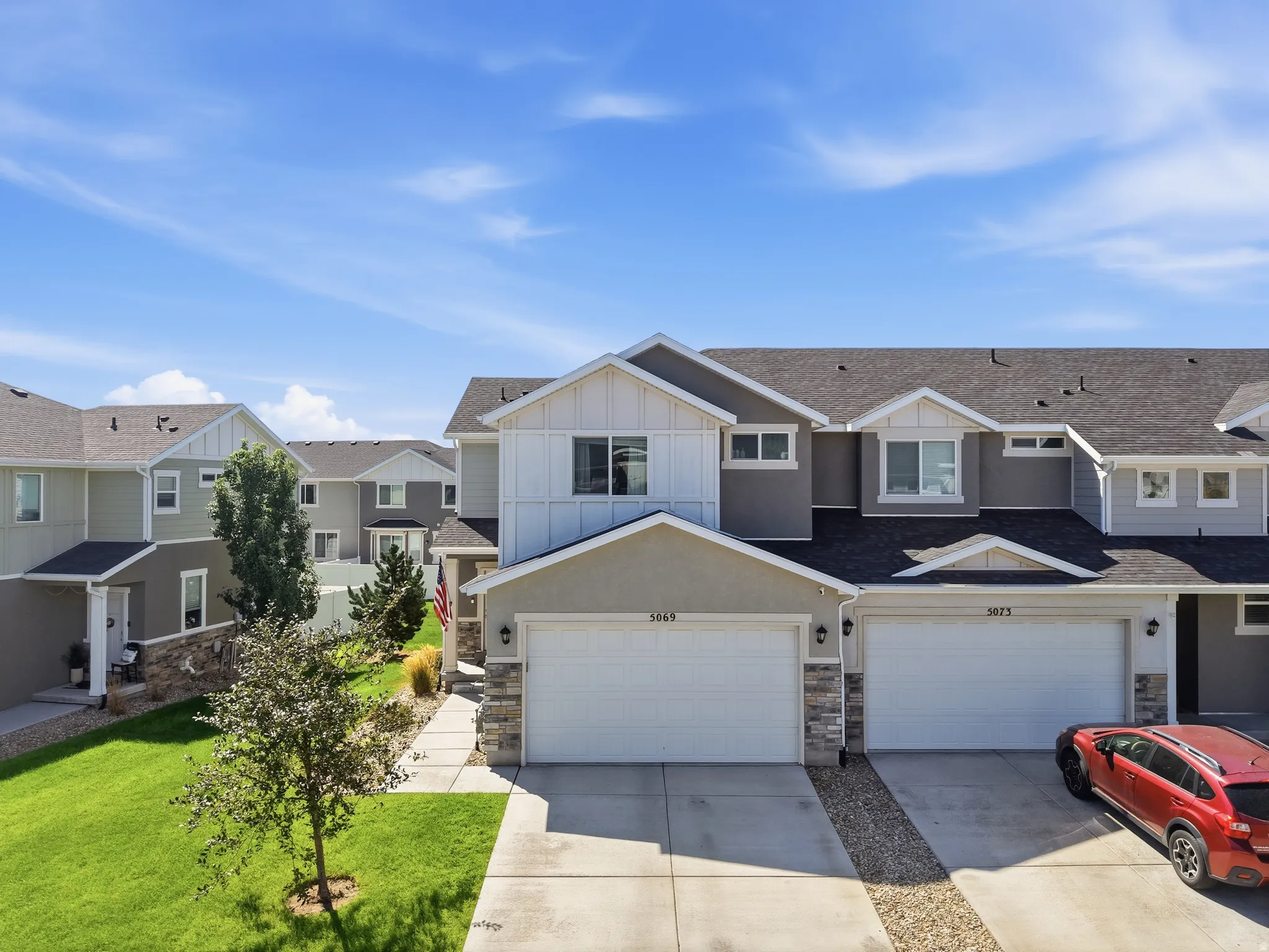 Contemporary architecture featuring multi-tone siding, stone accents, two-car garage, concrete driveway, and front lawn