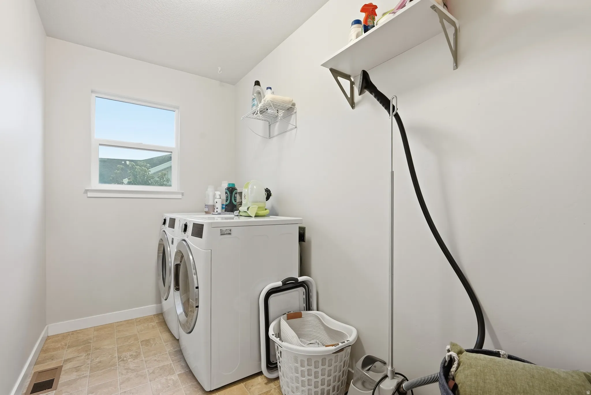 Bright laundry area featuring a window, light-toned walls, and a convenient wall-mounted shelf