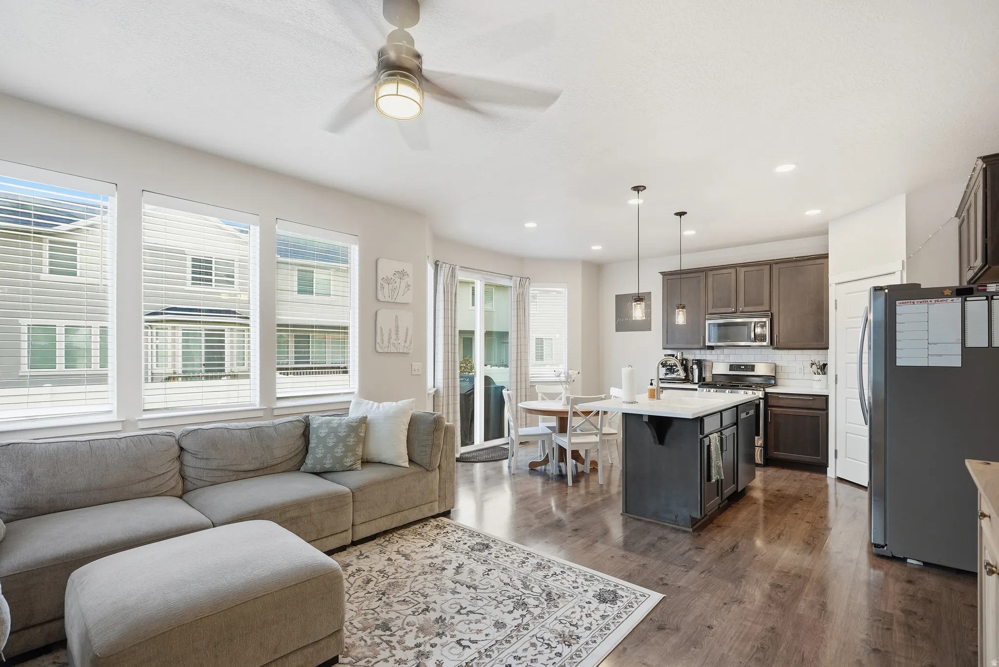 Recessed lighting, wood-finish flooring, stainless steel appliances, dark wood cabinetry, and a center island with white countertop