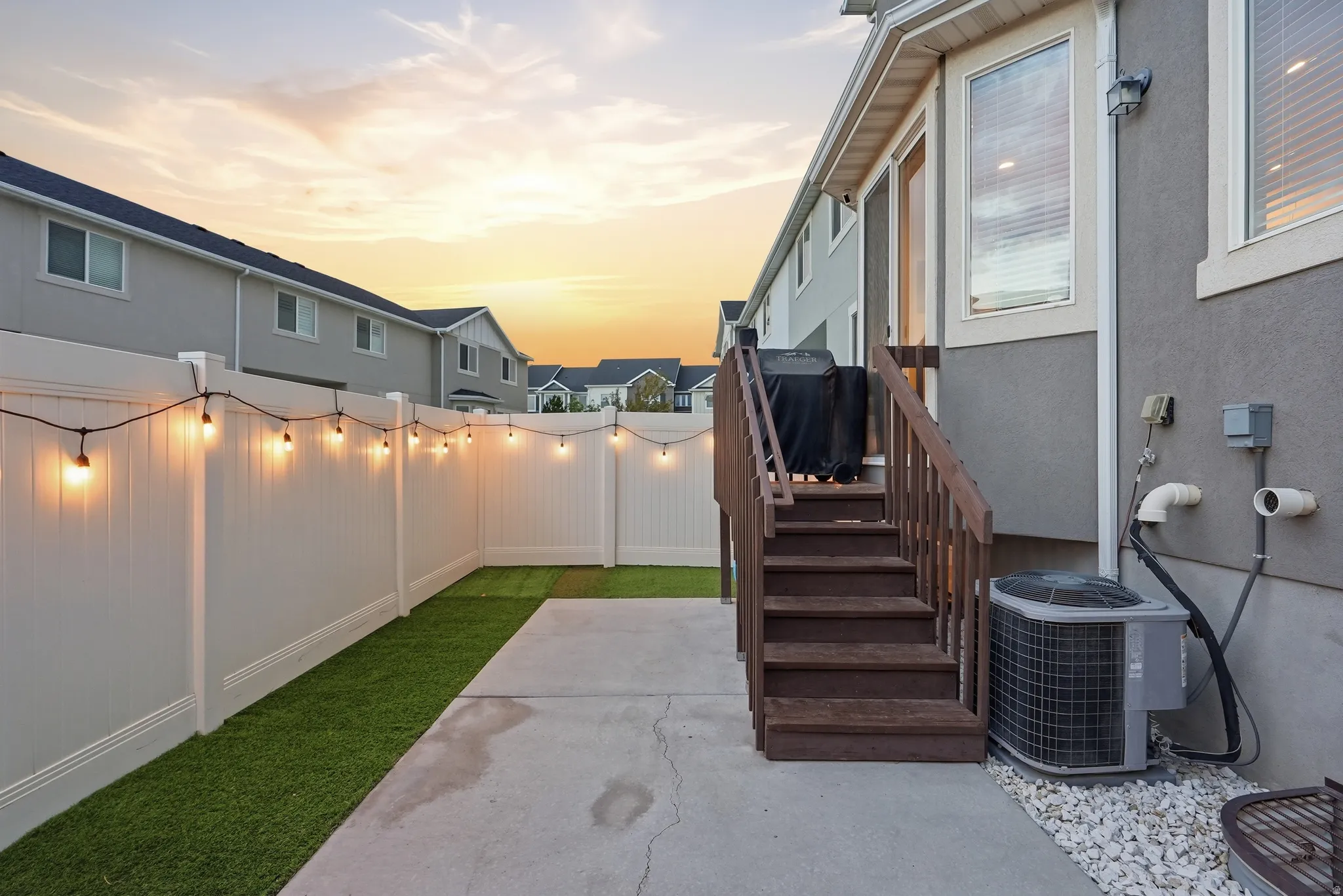 Private outdoor patio with string lighting, artificial turf, and a durable vinyl fence