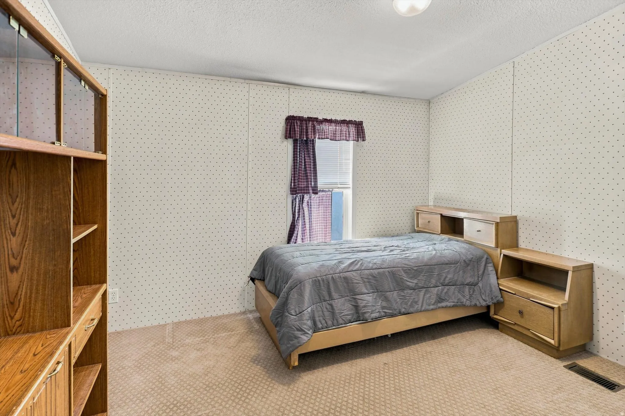 Wall-to-wall carpeting, textured ceiling, a window with blinds, and built-in shelving with glass-fronted cabinets