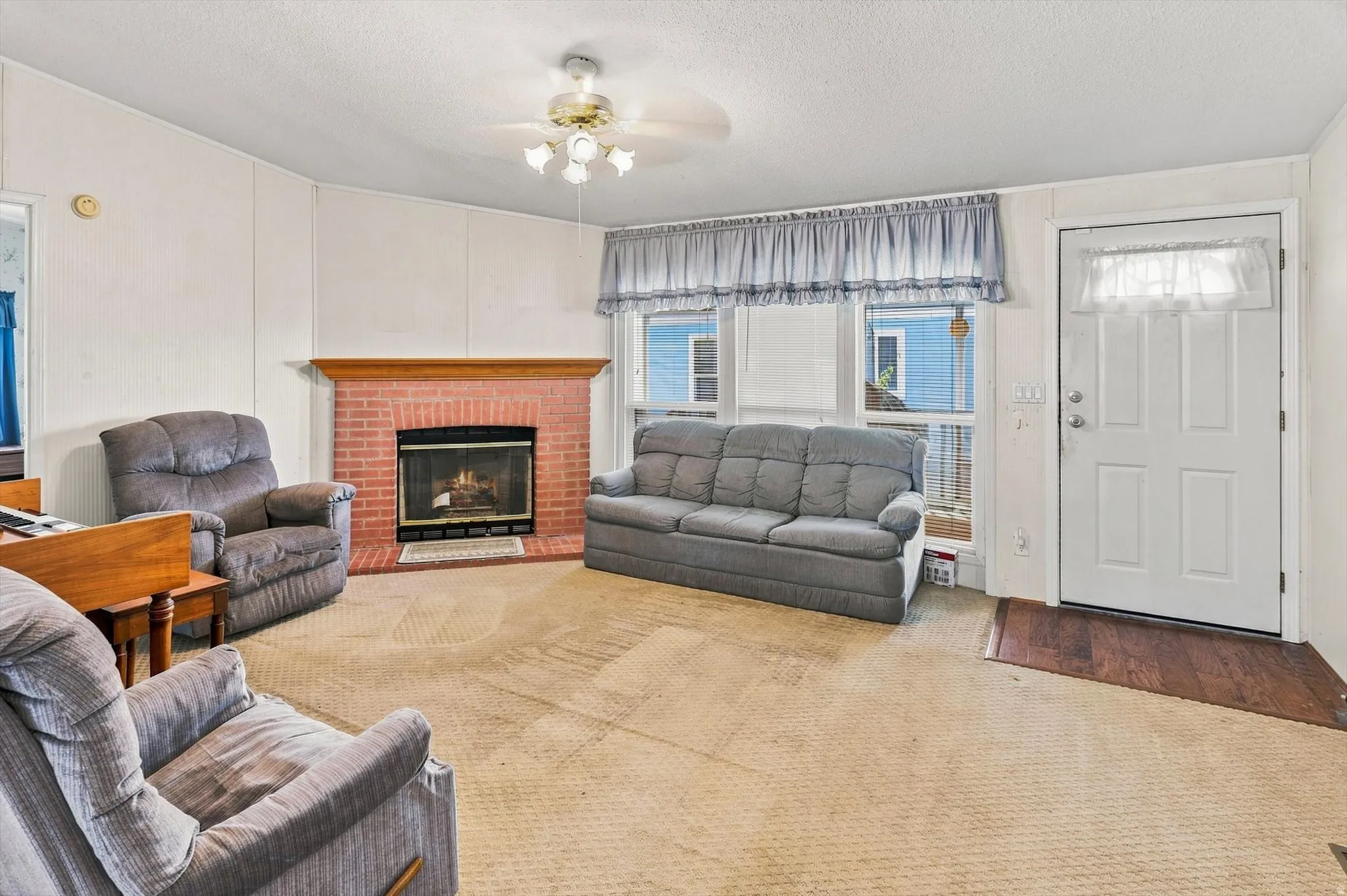 Brick fireplace with wood mantel, paneling, ceiling fan with light fixture, and front entry door with glass paneling