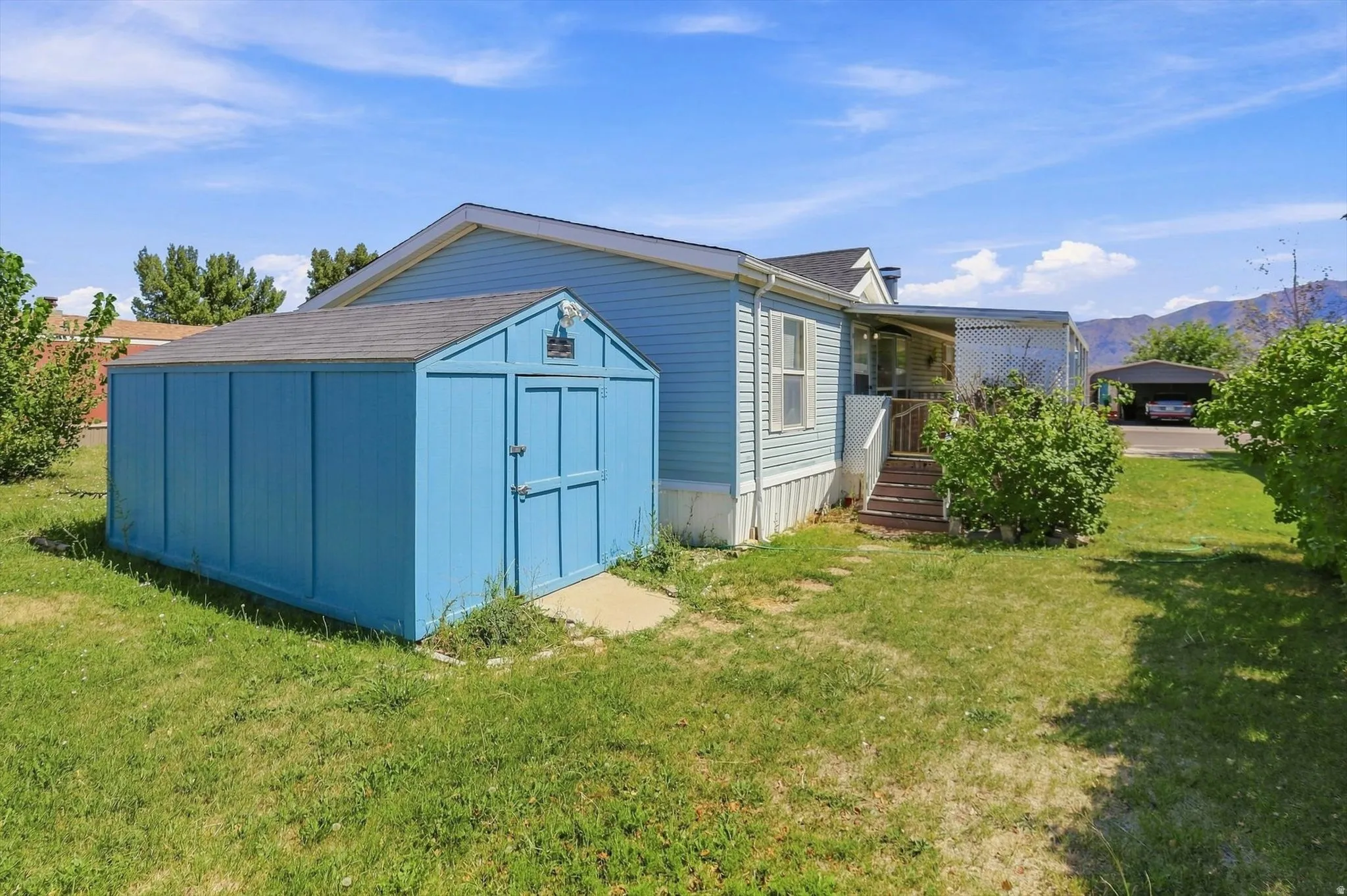 Spacious mobile home with attached storage shed featuring blue exterior siding and pitched roof design