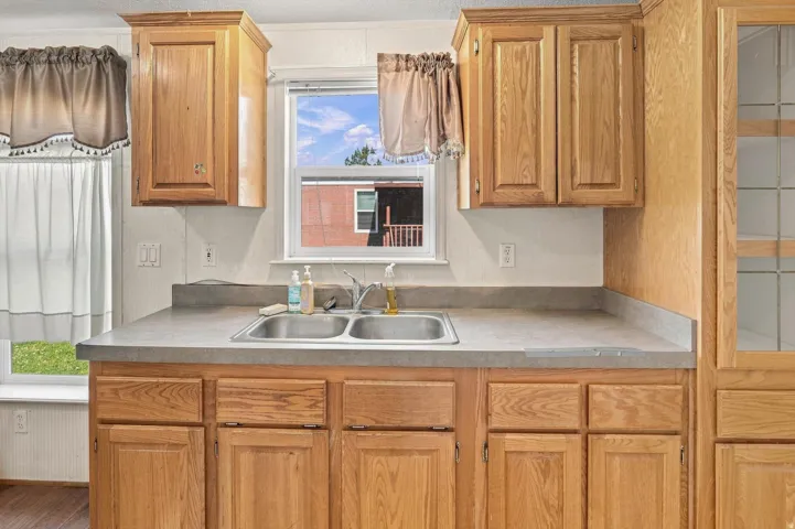 Galley kitchen featuring warm wood cabinetry with raised-panel doors, dual stainless steel sink with chrome faucet, laminate countertops, and ample under-cabinet storage