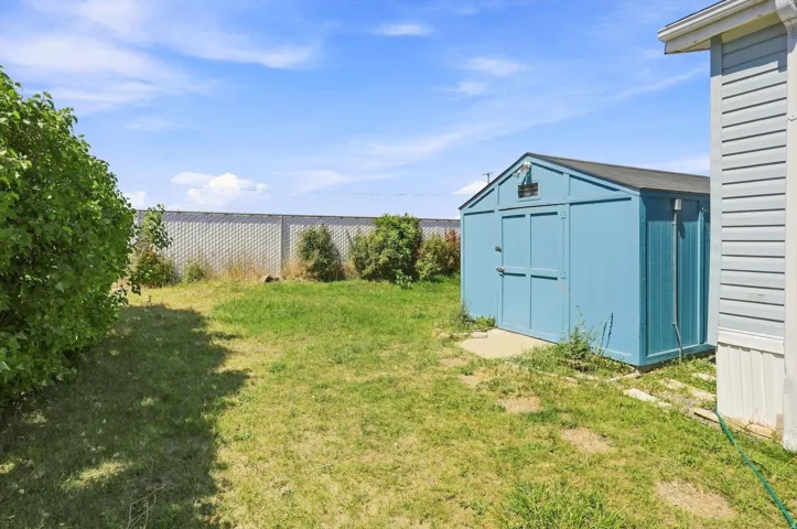 Expansive green space featuring a blue storage shed, concrete base, and perimeter fencing