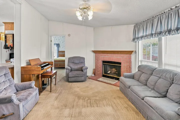 Living area featuring a brick fireplace with a wood mantle, large window, and ceiling fan with lighting