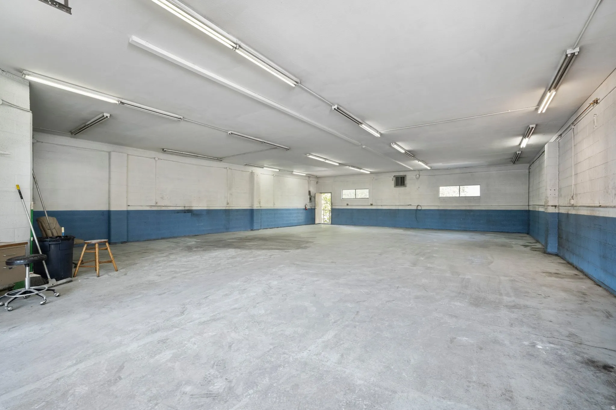 Expansive concrete flooring with a neutral wall palette, featuring multiple fluorescent light fixtures
