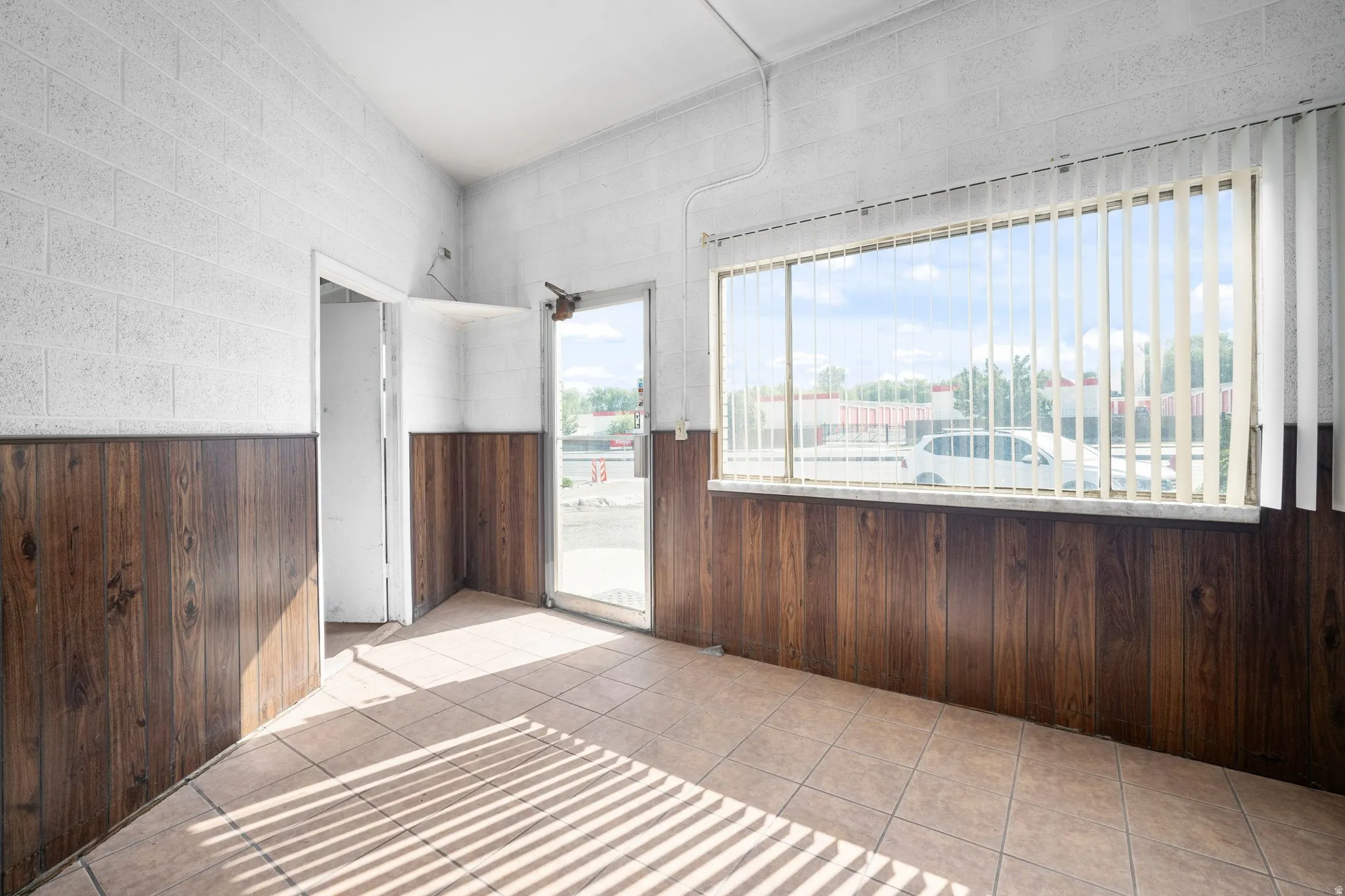 Tiled flooring throughout, wood-paneling accents, block wall construction, and a large window with vertical blinds