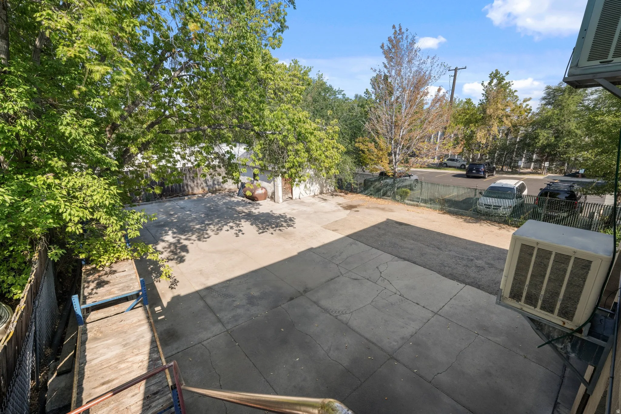 Paved outdoor area with surrounding mature trees and a chain-link fence