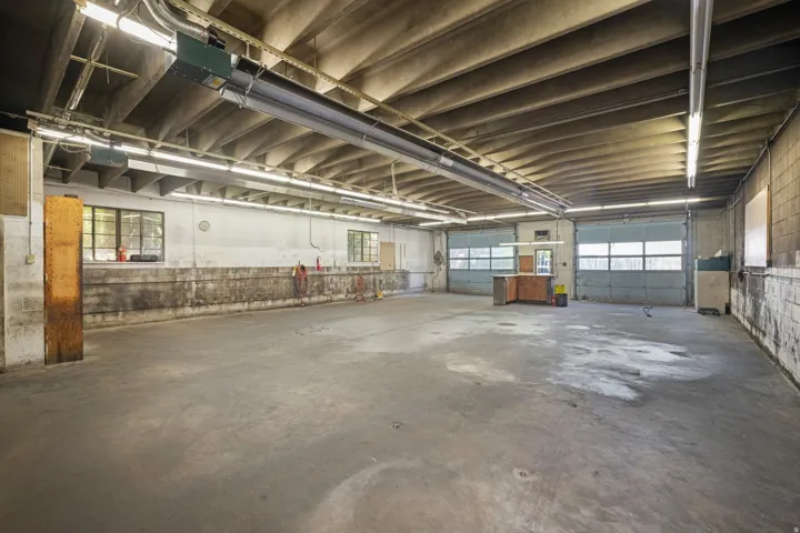Spacious concrete slab flooring, exposed ceiling with fluorescent lighting, multiple roll-up doors, and several windows