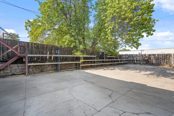 Paved exterior area with a perimeter fence, mature trees, and storage shelving