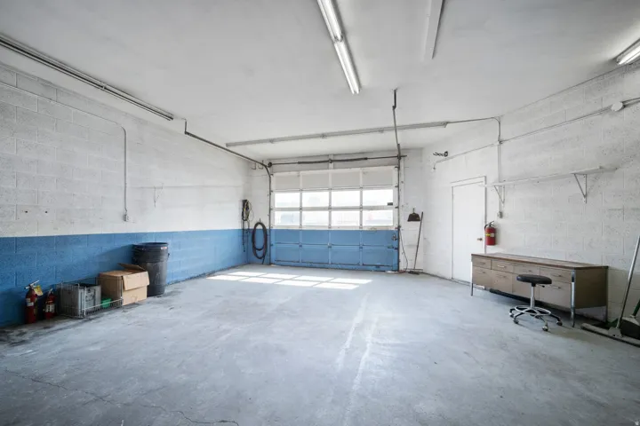 Concrete block walls, concrete flooring, overhead fluorescent lighting, roll-up garage door, and a utility door