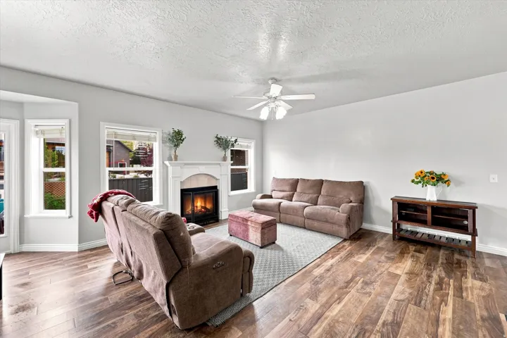 Recessed fireplace with an ornate white mantel, wood-finish flooring, and a ceiling fan