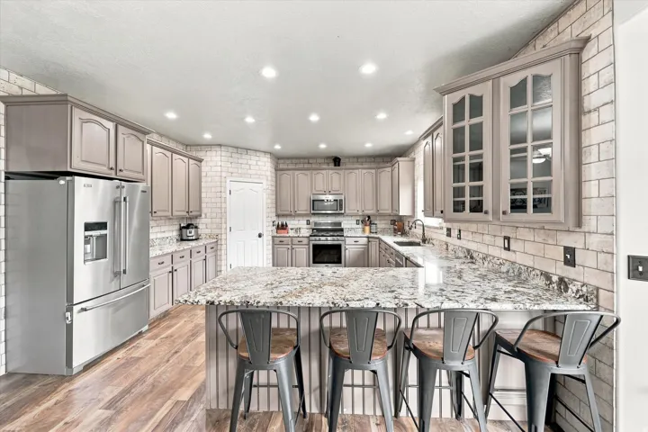 Kitchen featuring gray cabinetry, stainless steel appliances, a tile backsplash, and a granite-finish island with seating
