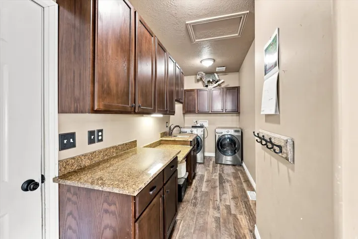 Wood-finish flooring, granite-style countertops, dark wood cabinetry, and a utility sink