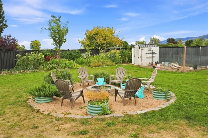Expansive backyard featuring a central fire pit area with gravel hardscaping and stone edging, surrounded by a lush green lawn