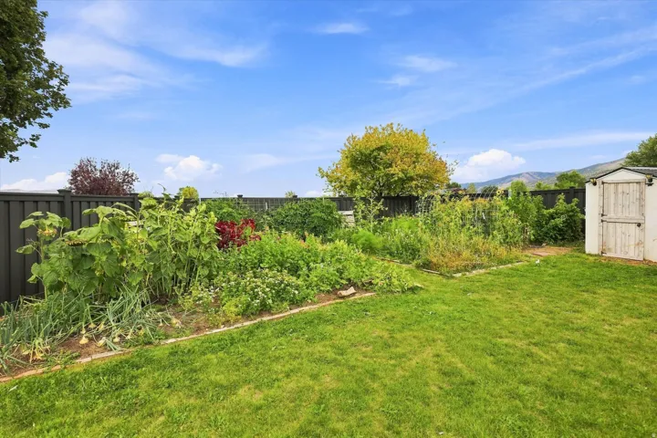 Expansive backyard featuring a manicured lawn, established garden beds, a privacy fence, and a storage shed