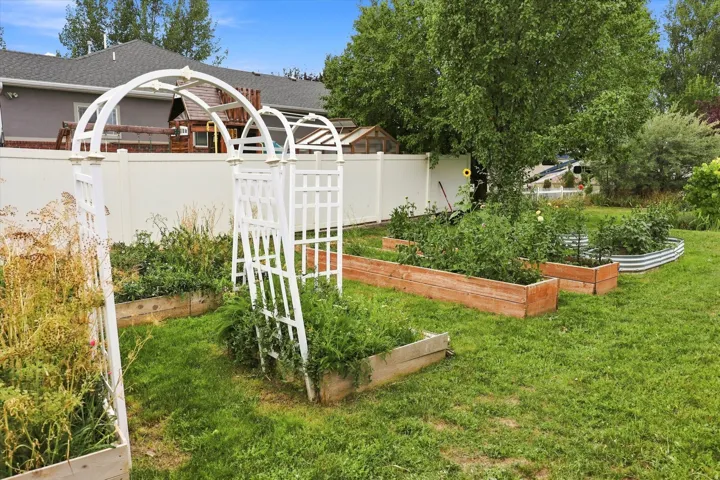 Manicured lawn with white privacy fencing, multiple raised garden beds, and two white garden arbors