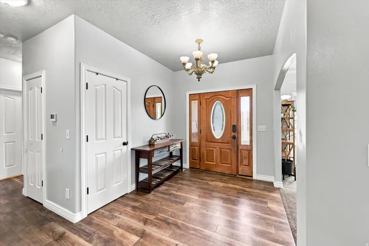 Wood-finish flooring, a solid wood entry door with oval glass insert and sidelights, an arched doorway, and a brass chandelier