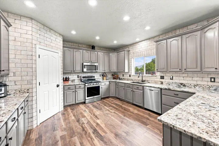 Kitchen featuring gray cabinetry, stainless steel appliances, speckled stone countertops, brick-finish wall cladding, and wood-finish flooring