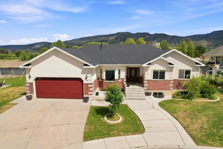 Stucco and brick exterior with a dark-pitched roof, featuring a two-car garage with a red door, a concrete driveway, and a paved walkway leading to the entrance