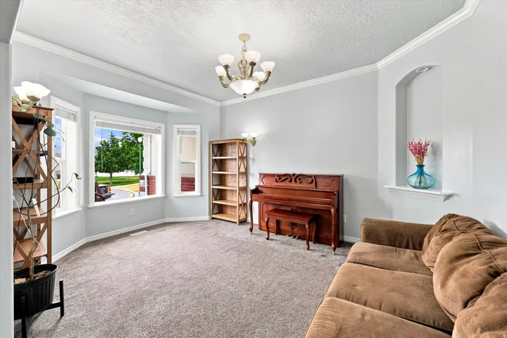 Bay window, crown molding, wall niche with integrated shelf, ceiling-mounted chandelier, and wall-to-wall carpeting